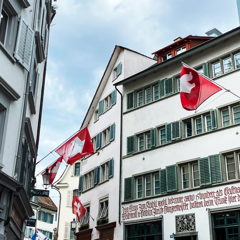 Old city centre of Swiss town Zurich. View of a street with Swiss flags placed on the traditional buildings.